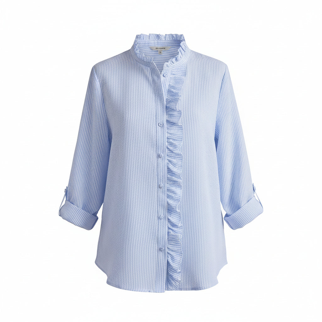 A woman wearing a light blue and white vertically striped button-up shirt with ruffle details on the front and collar, paired with light blue jeans, standing in a bright living room.