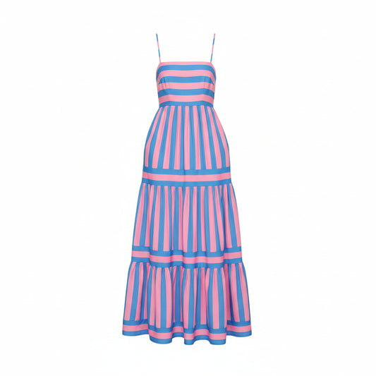 Woman wearing a pink and blue striped dress standing in a room with a vase of sunflowers.