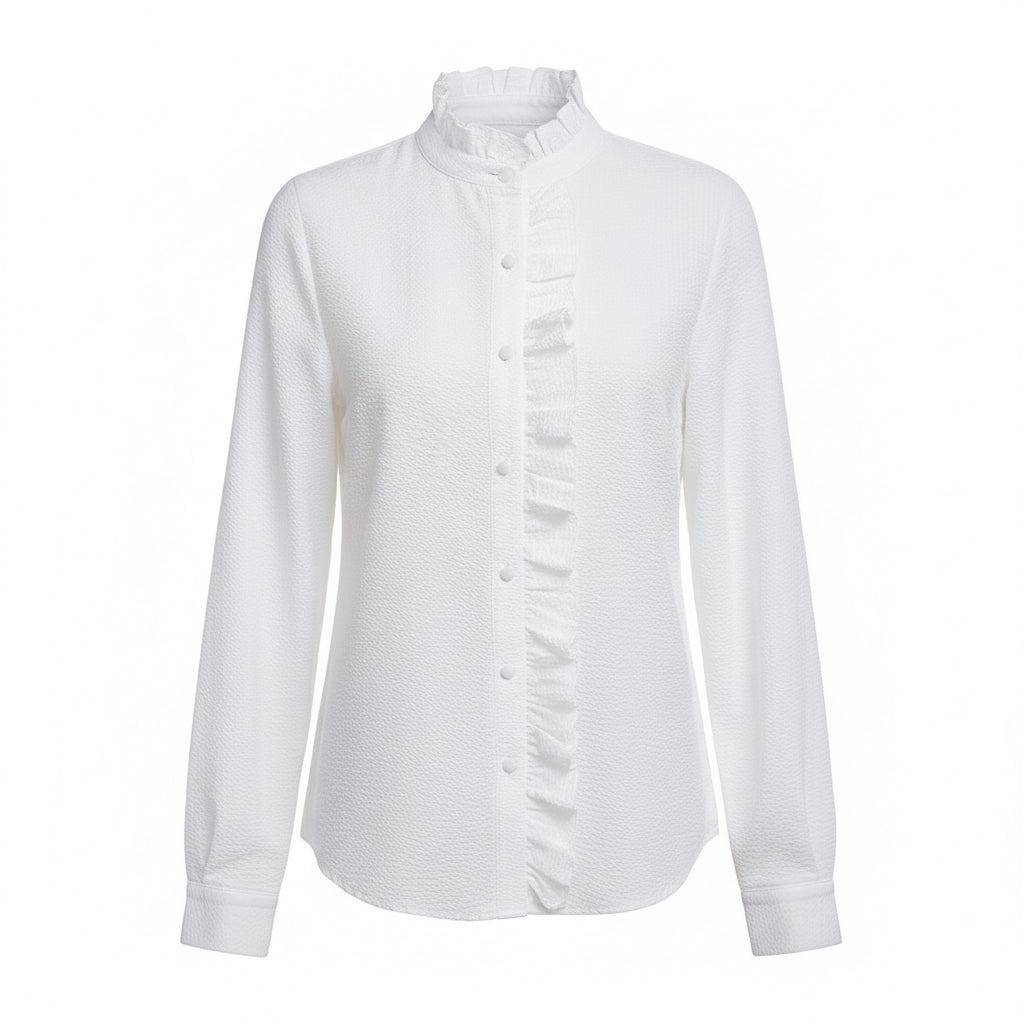 A woman wearing a white long-sleeve button-up blouse with a ruffled high collar and front placket, paired with light blue jeans, standing in a bright living room with a white sofa.