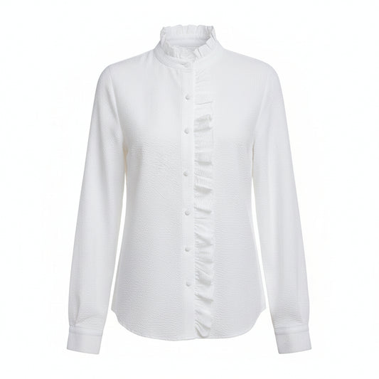 A woman wearing a white long-sleeve button-up blouse with a ruffled high collar and front placket, paired with light blue jeans, standing in a bright living room with a white sofa.